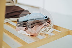 Stack of cotton tops in natural tones on wooden shelf in bright room