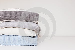 Stack of cozy comfortable homely clean washed knitted sweaters in pastel colors, laundry and washing clothes concept with copy