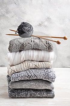 Stack of cozy knitted sweaters and pullovers with knitting needles on wooden background photo