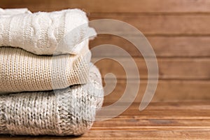 Stack of cozy knitted warm sweater ,wooden background . White Sweaters in retro Style