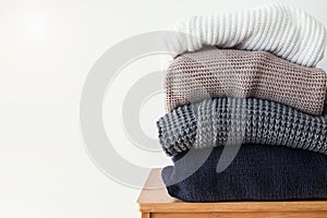 Stack of cozy winter sweaters on the white wall background.