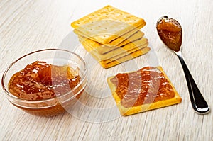 Stack of crackers, bowl with apple jam, spoon, sandwich from cookie with jam on table