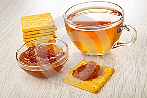 Stack of crackers, cup with tea, bowl with apple jam, cookie with jam on table