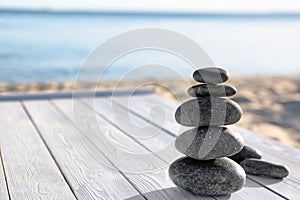 Stack of dark stones on wooden deck near sea. Zen concept