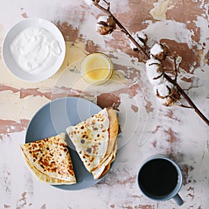 Stack of delicious homemade pancakes on plate with honey, sour cream and tea. Breakfast. Rustic style, close up top view. Flat lay