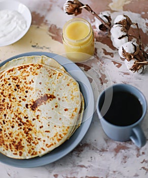 Stack of delicious homemade pancakes on plate with honey, sour cream and tea. Breakfast. Rustic style, close up top view. Flat lay