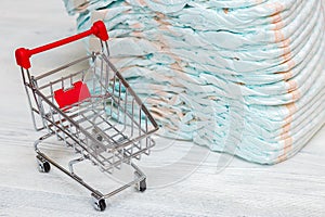 Stack of diapers or nappies and mini shopping cart, concept