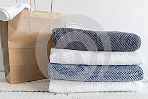 A stack of different bath towels near paper package on white wooden table. Spa and wellness, cotton terry textile