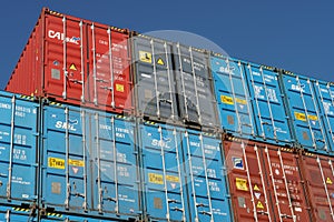 Stack of  different colors containers secured on the ship with one container with open door on the blue sky background.