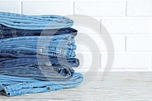 Stack of different jeans on white wooden table against wall. Space for text