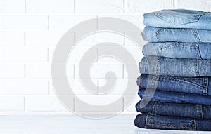 Stack of different jeans on white wooden table against wall. Space for text