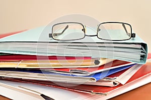 Stack of document file folders with glasses on the brown wooden office desk