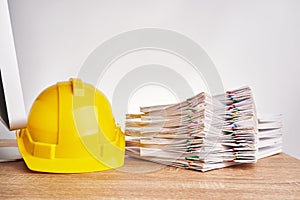 Stack document with yellow engineer hat on wooden computer table