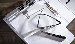 Stack of documents, eyeglasses and pen on table in office