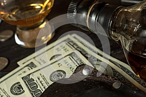 A stack of dollars, leather wallet and a bottle of whisky on a table