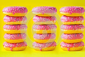 A stack of donuts with pink icing on a yellow background side view. Junk food. Sweets, pastries. Calories, fat