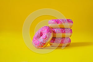 A stack of donuts with pink icing on a yellow background side view. Junk food. Sweets, pastries. Calories, fat