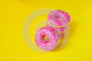 A stack of donuts with pink icing on a yellow background side view. Junk food. Sweets, pastries. Calories, fat.