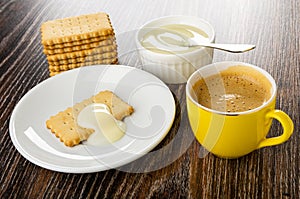 Dry cookies, spoon in small bowl with condensed milk, cookie poured milk in saucer, coffee espresso in cup on wooden table