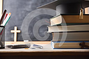 Stack of educational books and a mortarboard on desk