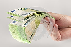 Stack of euro bills in hand. A large stack of 100 euro banknotes in a male hand on a uniform gray background. The