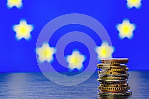 A stack of euro coins of different denominations on the background of the flag of the European Union