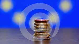 A stack of euro coins of different denominations on the background of the flag of the European Union