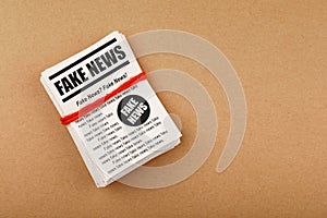 Stack of FAKE NEWS newspapers over brown paper