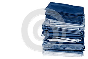 Stack of folded clean blue bedding on a white background: duvet covers, sheets, pillowcases. Close-up. Copy space