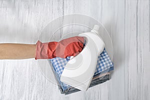 Stack of folded clothes and detergent bottle in female hand. Housework