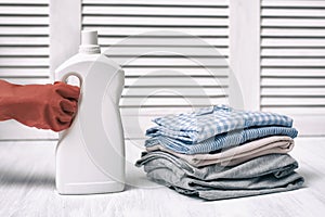 Stack of folded clothes and detergent bottle in female hand. Housework
