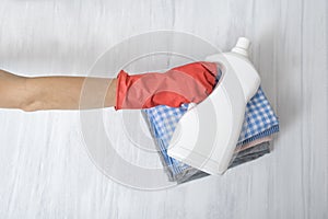Stack of folded clothes and detergent bottle in female hand. Housework
