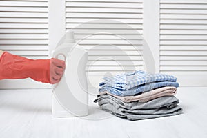 Stack of folded clothes and detergent bottle in female hand. Housework