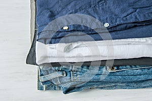 Stack of Folded Cotton Pants Shirts Jeans on White Wood Background Shelf. Eco Fashion Authentic Classic Unisex Style