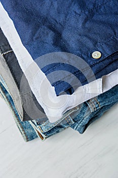 Stack of Folded Cotton Pants Shirts Jeans on White Wood Background Shelf. Eco Fashion Authentic Classic Unisex Style Natural