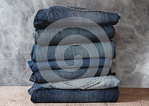 Stack of folded jeans on shelf against gray wall. Closeup of denim in different colors