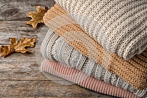 Stack of folded knitted sweaters and autumn leaves