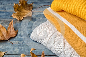 Stack of folded knitted sweaters and autumn leaves on table.