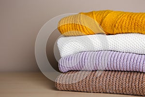 Stack of folded knitted sweaters on wooden table, closeup. Space for text