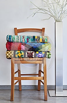 Stack of folded traditional quilts on wooden chair, floor lamp