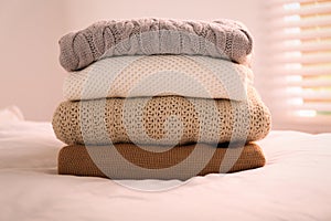 Stack of folded warm sweaters on bed indoors