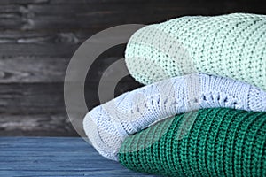 Stack of folded warm sweaters on blue table. Space for text