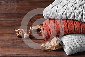 Stack of folded warm sweaters and leaves on wood