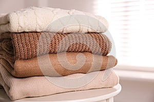 Stack of folded warm sweaters on white table indoors, closeup