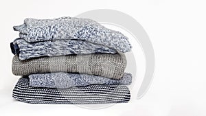 Stack of folded woolen knitwear on white background. Season of warm knitted clothes: sweaters, jumpers, cardigans