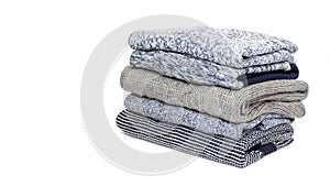 Stack of folded woolen knitwear on white background: sweaters, jumpers in grey and blue tone. Winter wardrobe concept