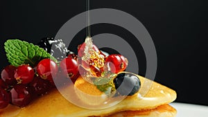 Stack of fresh fluffy pancakes decorated on top with forest berries on plate and pouring honey syrup. Delicious, healthy