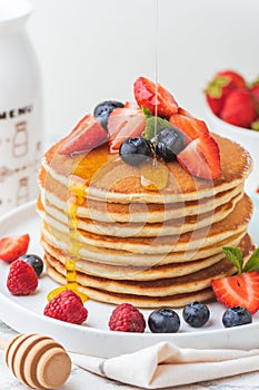 Stack of fresh pancakes with strawberries and blueberries drizzled with maple syrup and honey. Healthy traditional American