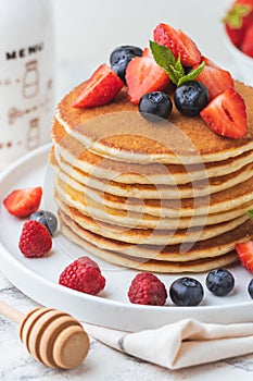 Stack of fresh pancakes with strawberries and blueberries drizzled with maple syrup and honey. Healthy traditional American