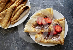 Stack of fresh thin pancakes with chocolate paste and strawberry on gray background